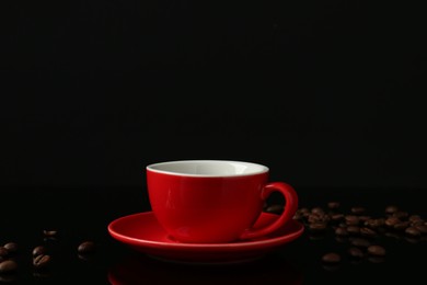 Photo of Red cup with coffee and roasted beans on black background, space for text