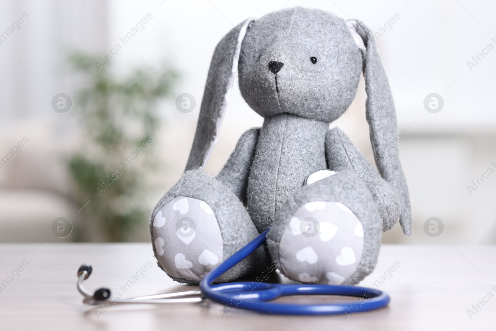 Photo of Pediatrics concept. Toy bunny with stethoscope on table indoors