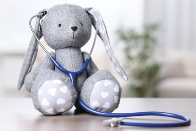 Photo of Pediatrics concept. Toy bunny with stethoscope on table indoors, space for text