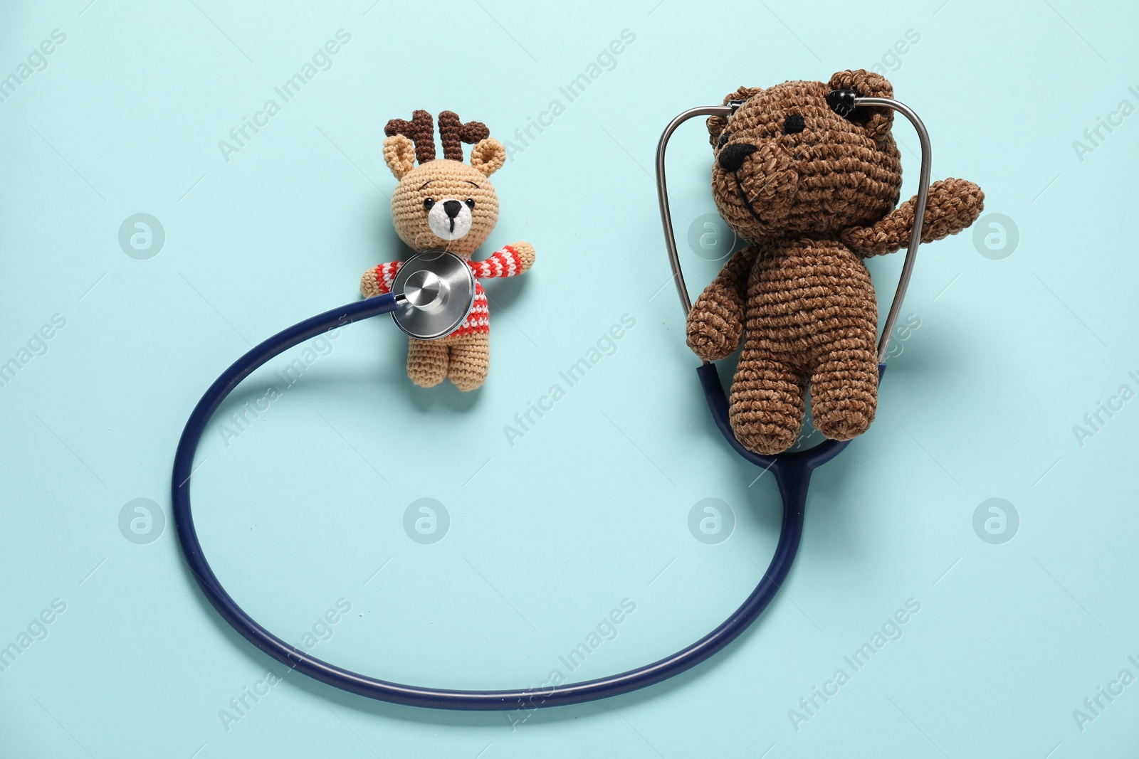 Photo of Pediatrics concept. Toy bear and deer with stethoscope on light blue background, flat lay