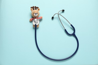 Photo of Pediatrics concept. Toy deer with stethoscope on light blue background, top view