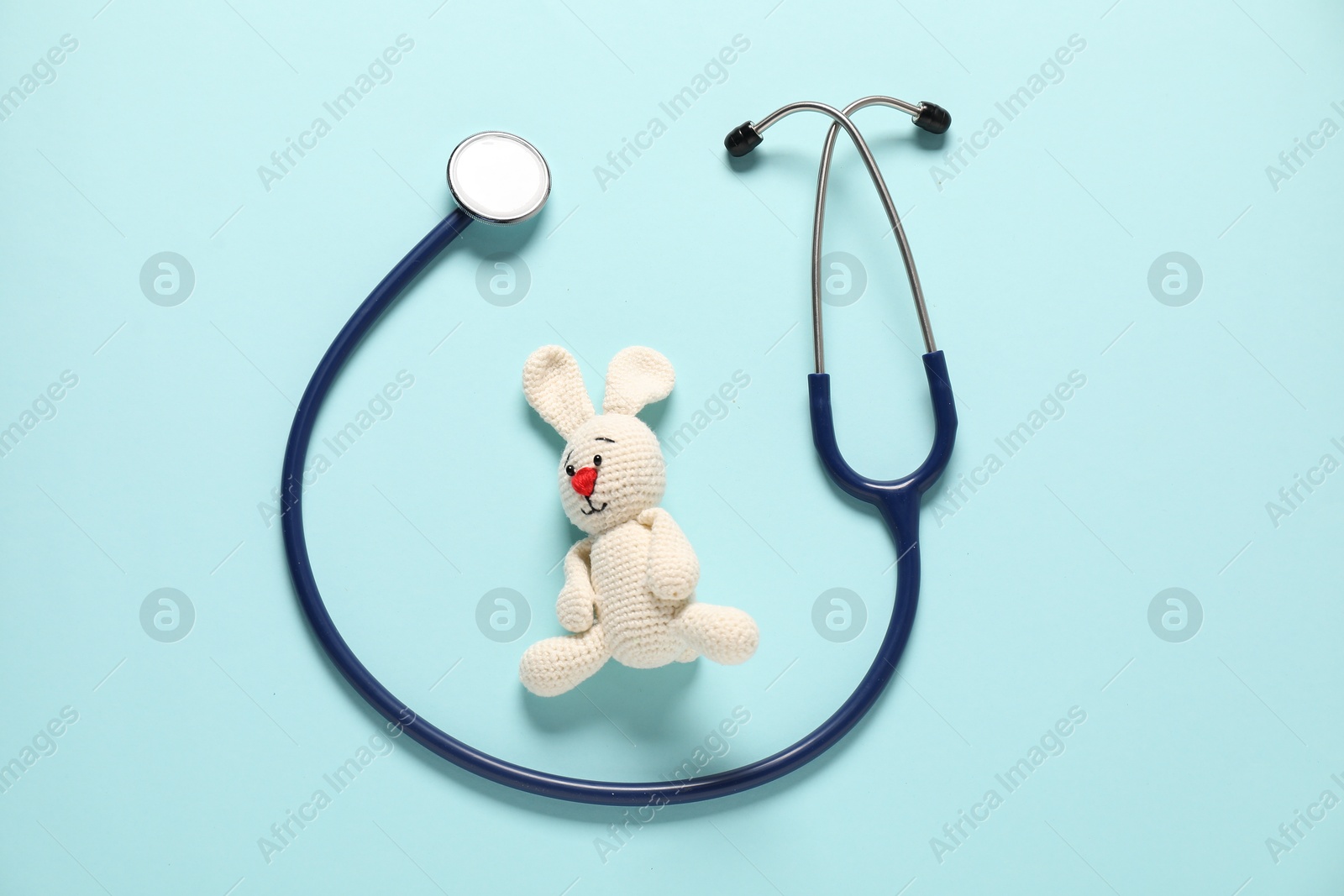 Photo of Pediatrics concept. Toy bunny with stethoscope on light blue background, top view