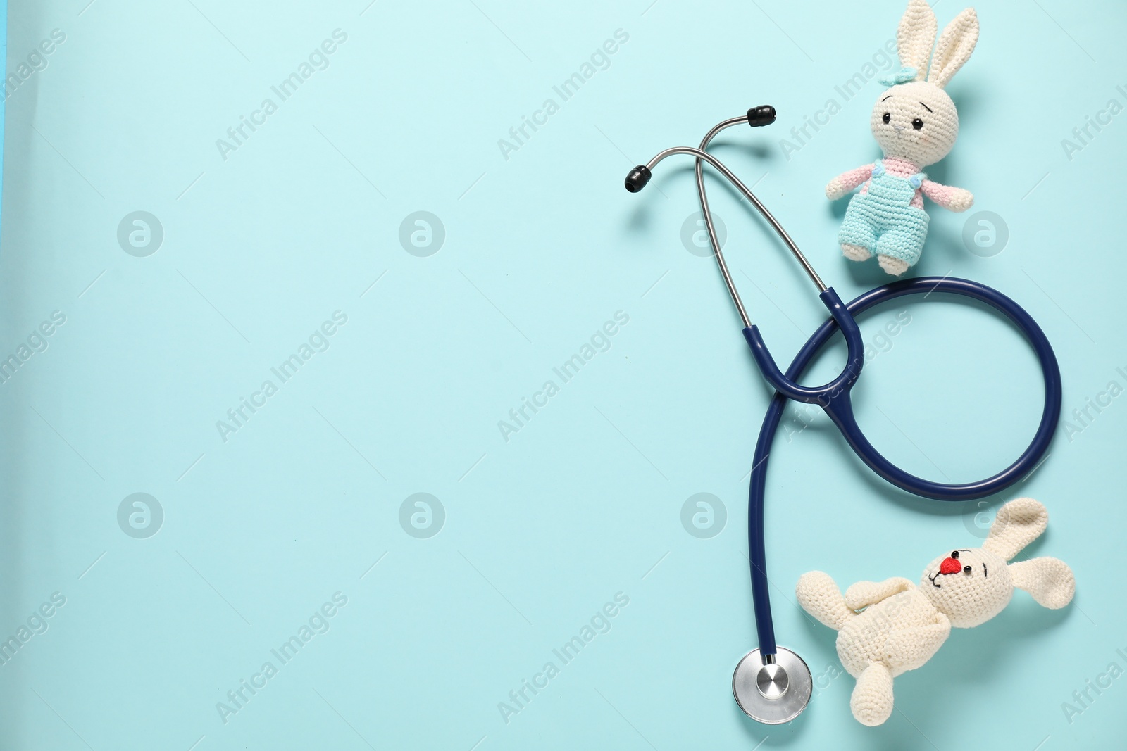 Photo of Pediatrics concept. Toy bunnies with stethoscope on light blue background, flat lay. Space for text