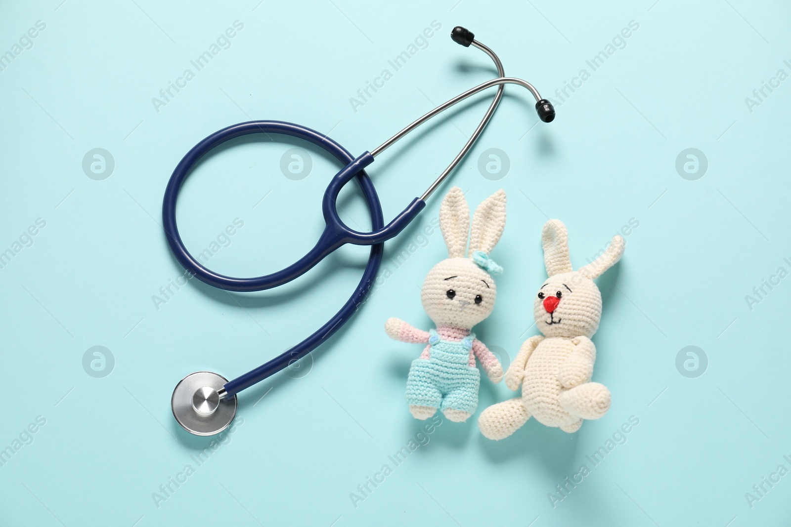 Photo of Pediatrics concept. Toy bunnies with stethoscope on light blue background, flat lay