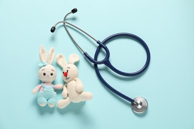 Photo of Pediatrics concept. Toy bunnies with stethoscope on light blue background, flat lay