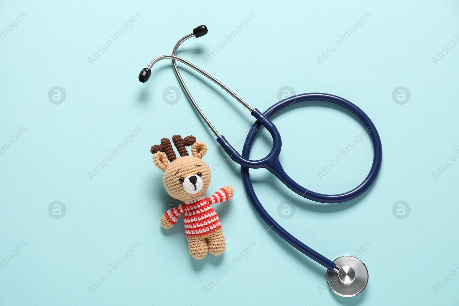 Photo of Pediatrics concept. Toy deer with stethoscope on light blue background, top view