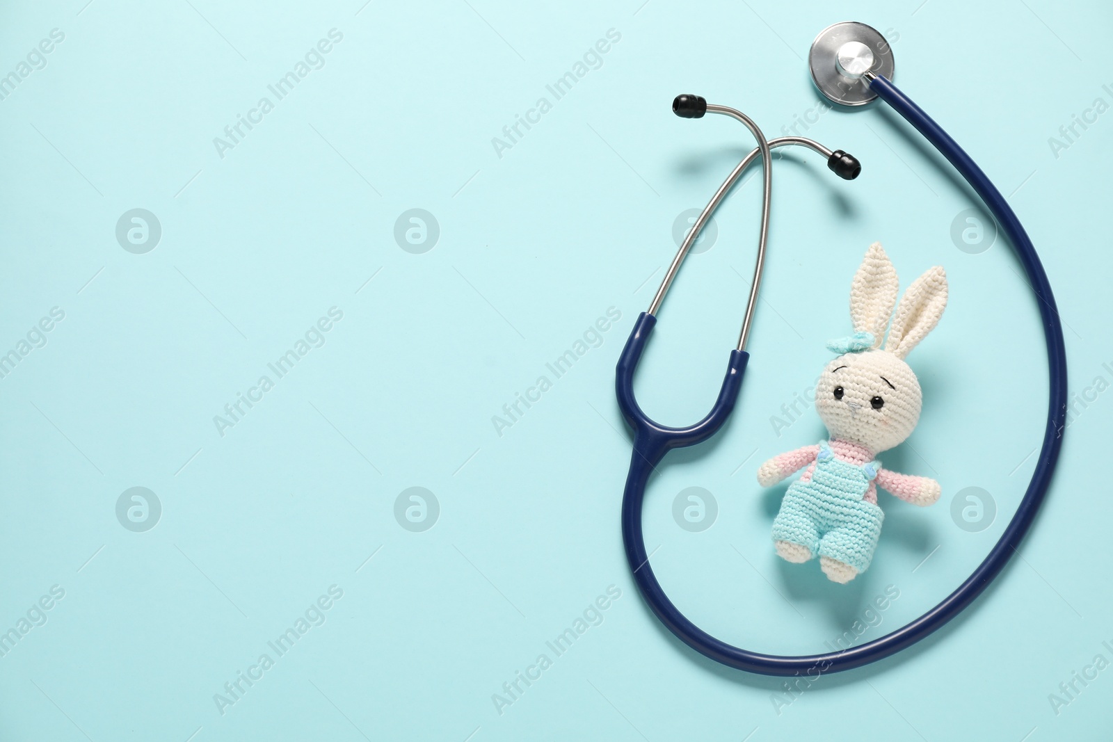 Photo of Pediatrics concept. Toy bunny with stethoscope on light blue background, top view. Space for text