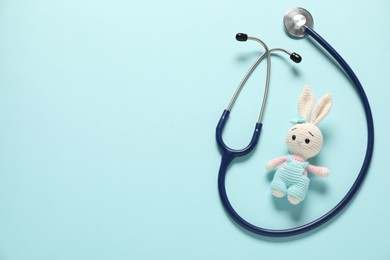 Photo of Pediatrics concept. Toy bunny with stethoscope on light blue background, top view. Space for text