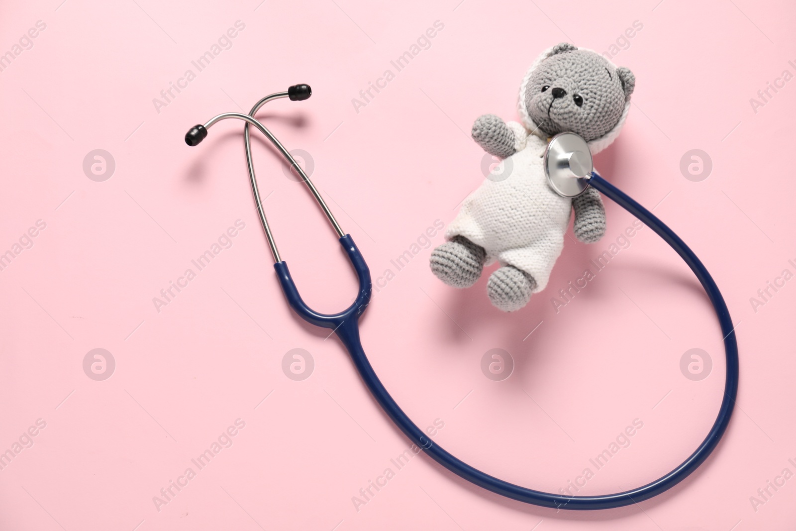 Photo of Pediatrics concept. Toy bear with stethoscope on pink background, top view. Space for text