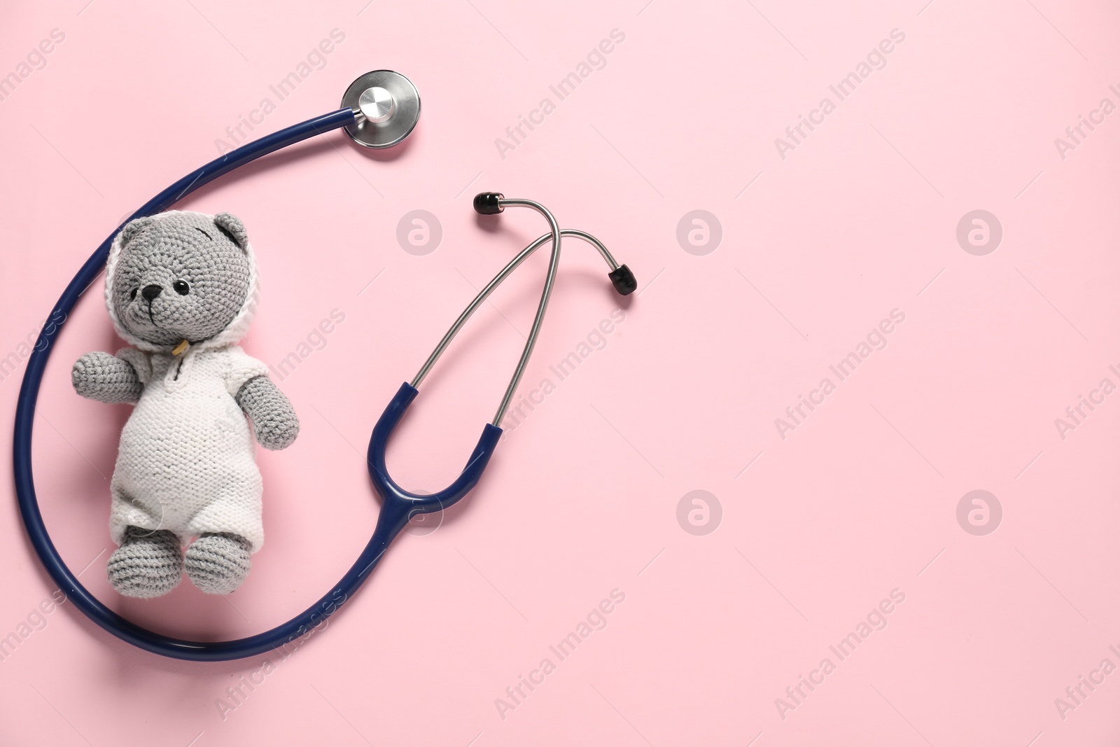 Photo of Pediatrics concept. Toy bear with stethoscope on pink background, top view. Space for text