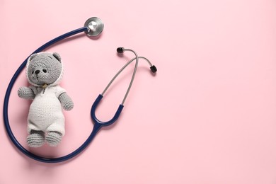 Photo of Pediatrics concept. Toy bear with stethoscope on pink background, top view. Space for text