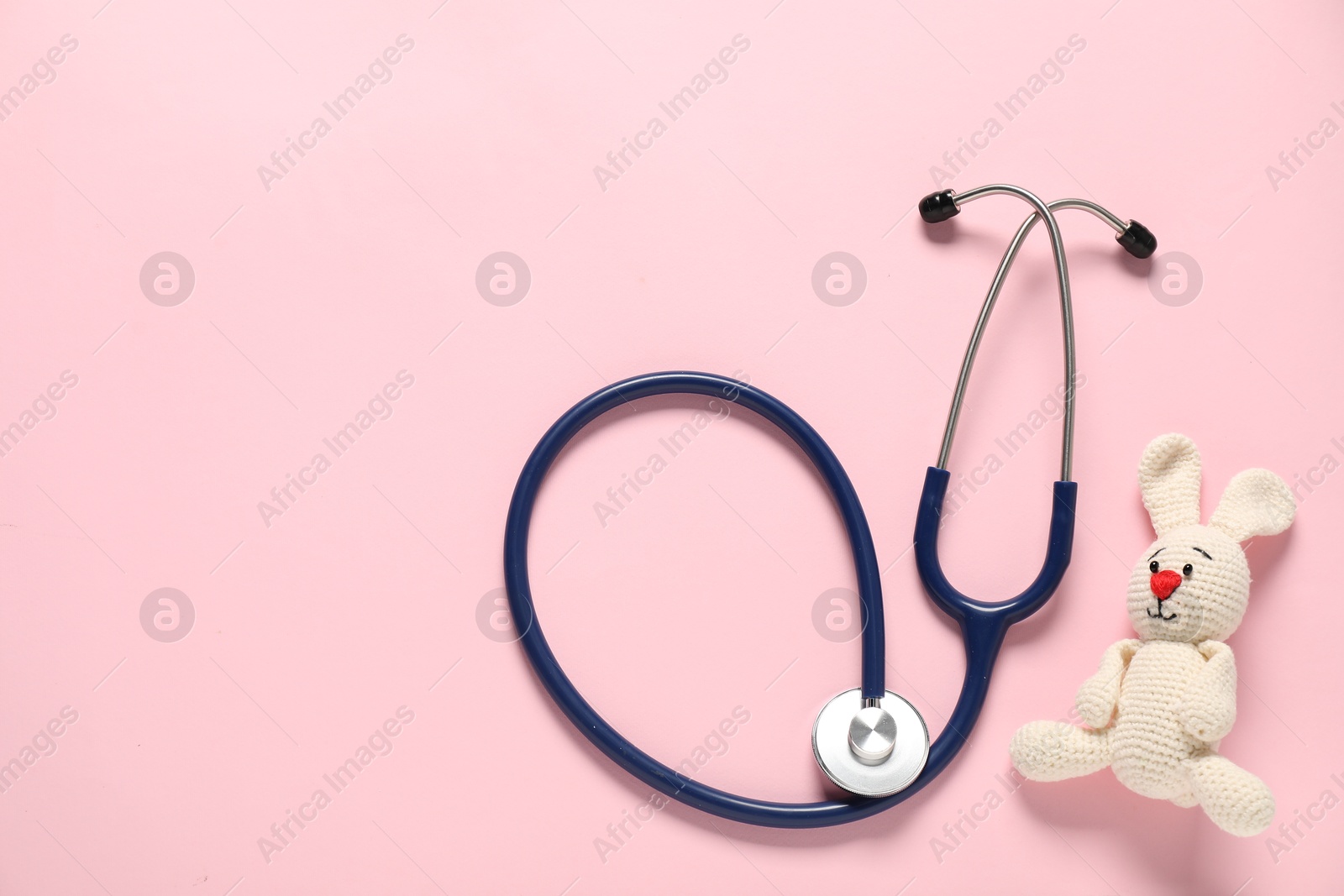 Photo of Pediatrics concept. Toy bunny with stethoscope on pink background, top view. Space for text