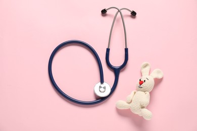 Photo of Pediatrics concept. Toy bunny with stethoscope on pink background, top view