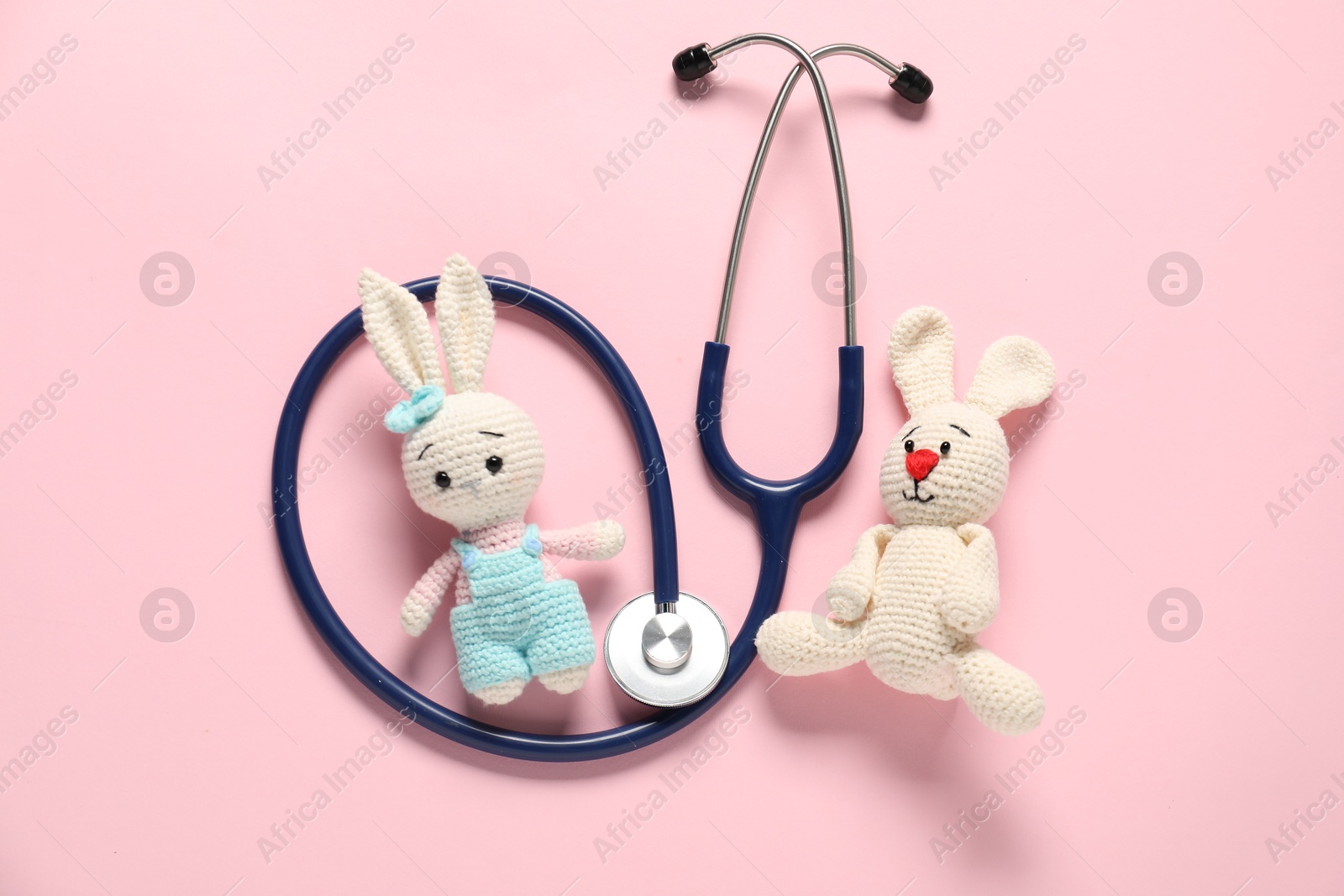 Photo of Pediatrics concept. Toy bunnies with stethoscope on pink background, flat lay