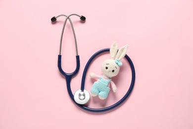 Photo of Pediatrics concept. Toy bunny with stethoscope on pink background, top view