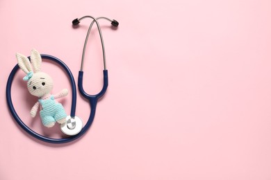 Photo of Pediatrics concept. Toy bunny with stethoscope on pink background, top view. Space for text