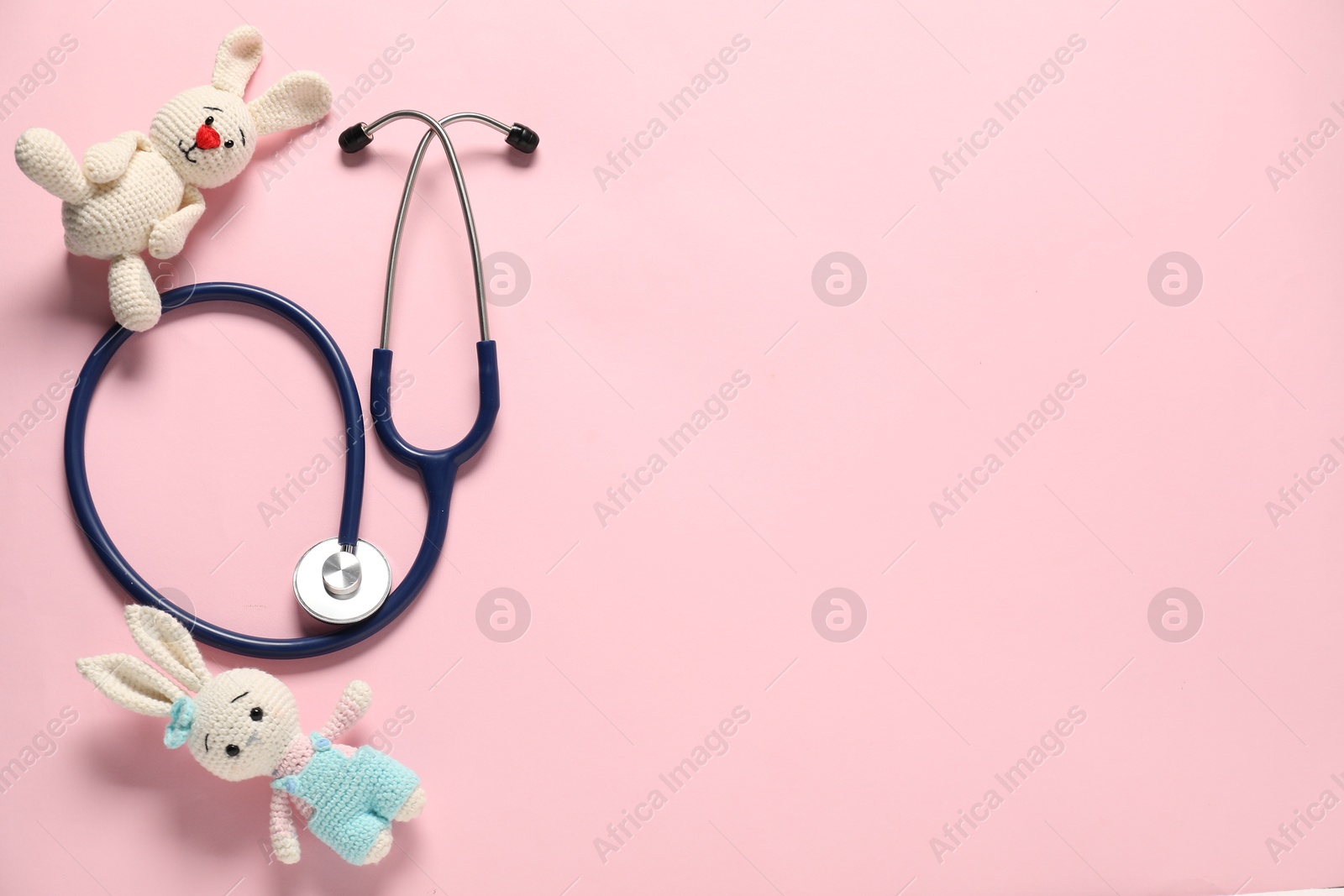 Photo of Pediatrics concept. Toy bunnies with stethoscope on pink background, flat lay. Space for text