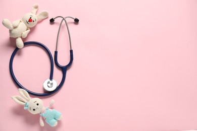 Photo of Pediatrics concept. Toy bunnies with stethoscope on pink background, flat lay. Space for text