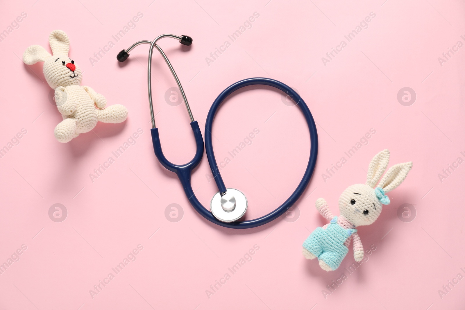 Photo of Pediatrics concept. Toy bunnies with stethoscope on pink background, flat lay