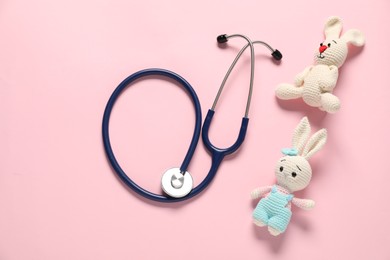 Photo of Pediatrics concept. Toy bunnies with stethoscope on pink background, flat lay