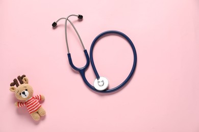 Photo of Pediatrics concept. Toy deer with stethoscope on pink background, top view