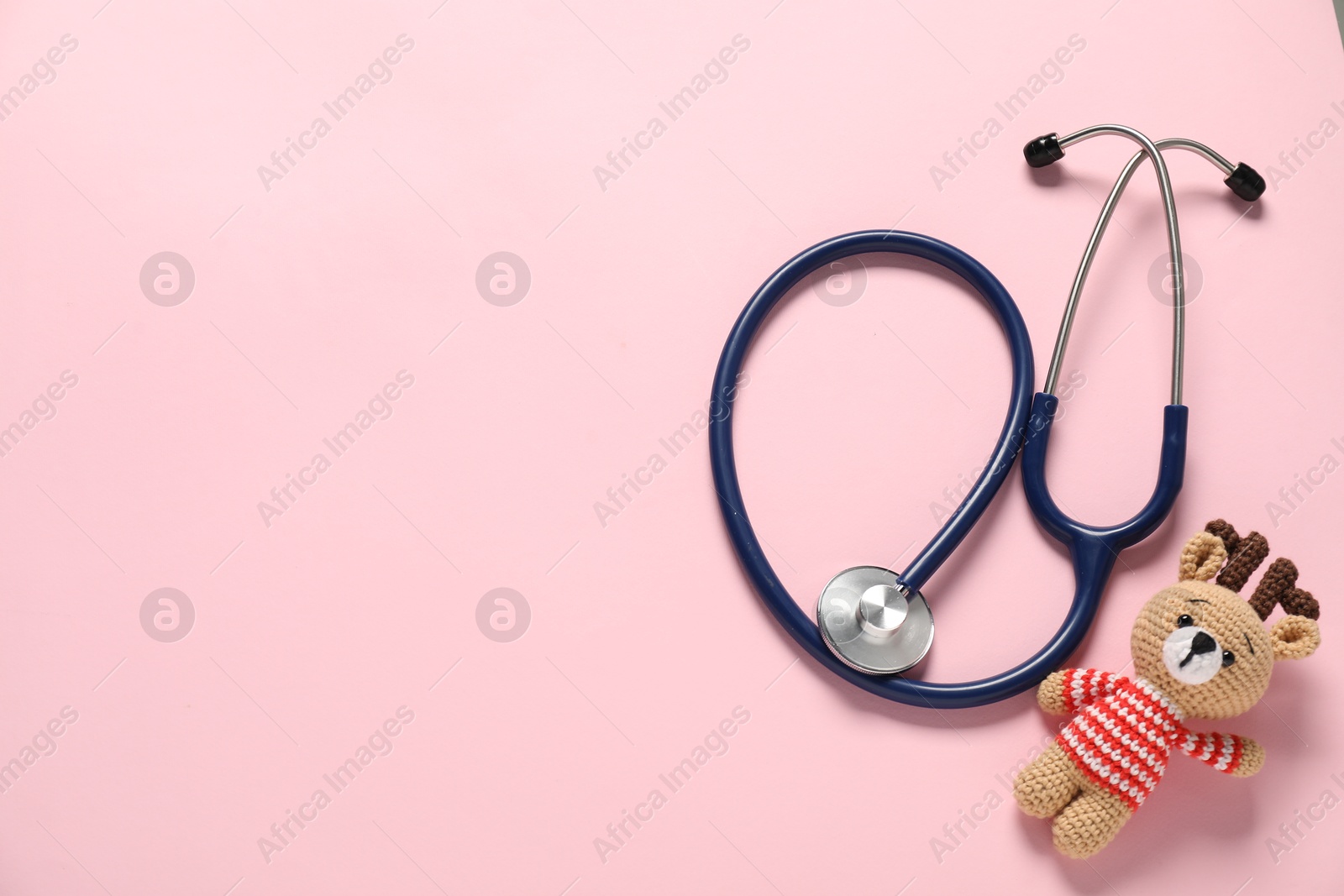 Photo of Pediatrics concept. Toy deer with stethoscope on pink background, top view. Space for text