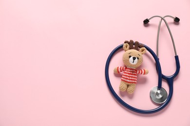 Photo of Pediatrics concept. Toy deer with stethoscope on pink background, top view. Space for text