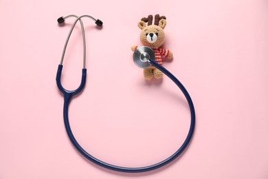 Photo of Pediatrics concept. Toy deer with stethoscope on pink background, top view