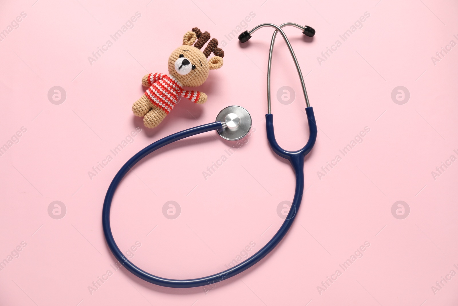 Photo of Pediatrics concept. Toy deer with stethoscope on pink background, top view