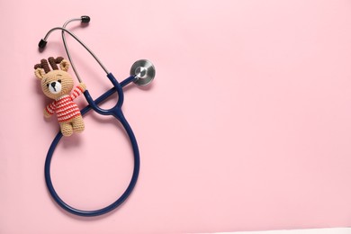 Photo of Pediatrics concept. Toy deer with stethoscope on pink background, top view. Space for text