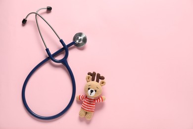 Photo of Pediatrics concept. Toy deer with stethoscope on pink background, top view. Space for text