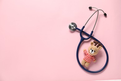 Photo of Pediatrics concept. Toy deer with stethoscope on pink background, top view