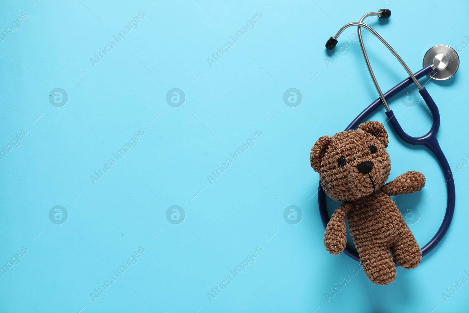 Photo of Pediatrics concept. Toy bear with stethoscope on light blue background, top view. Space for text