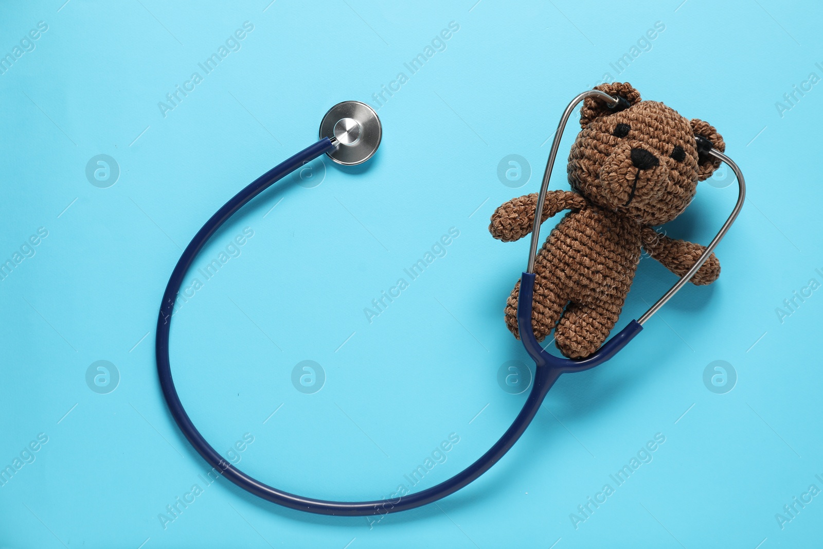 Photo of Pediatrics concept. Toy bear with stethoscope on light blue background, top view