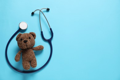 Photo of Pediatrics concept. Toy bear with stethoscope on light blue background, top view. Space for text