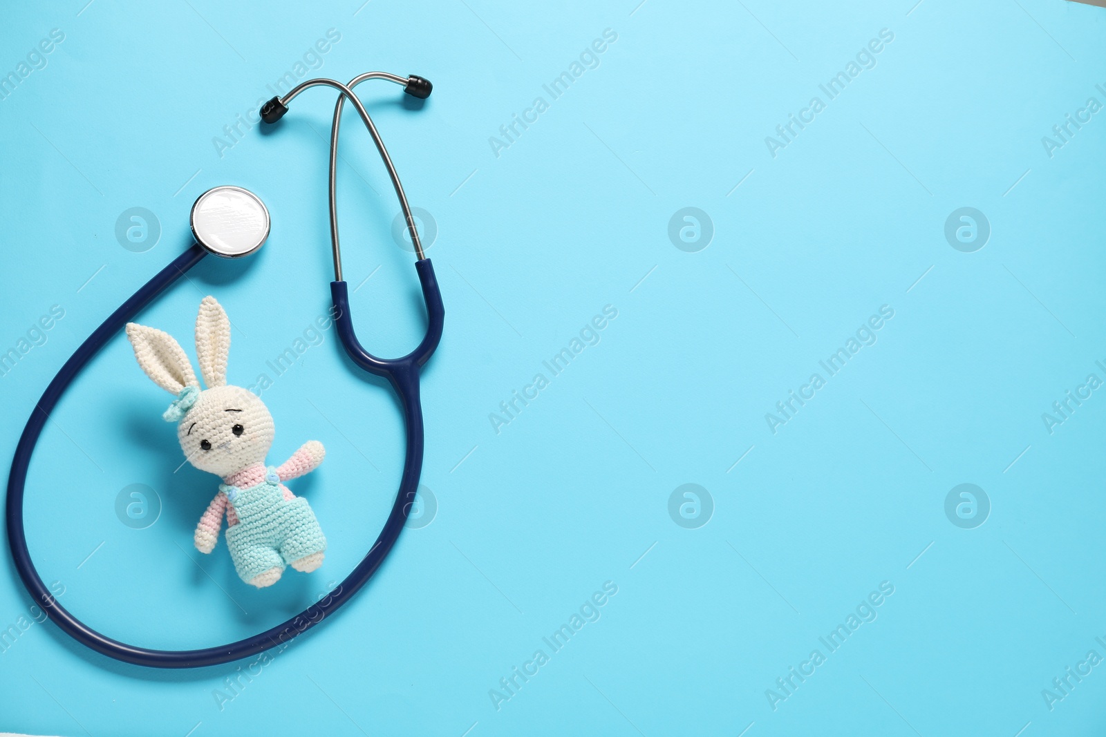 Photo of Pediatrics concept. Toy bunny with stethoscope on light blue background, top view. Space for text