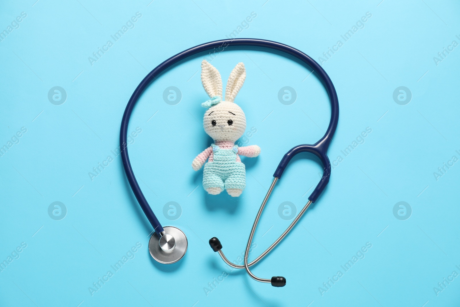 Photo of Pediatrics concept. Toy bunny with stethoscope on light blue background, top view