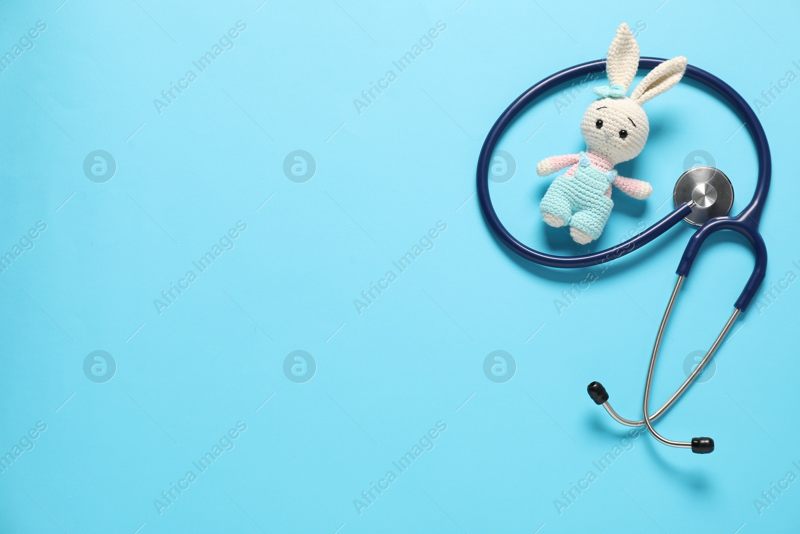 Photo of Pediatrics concept. Toy bunny with stethoscope on light blue background, top view. Space for text