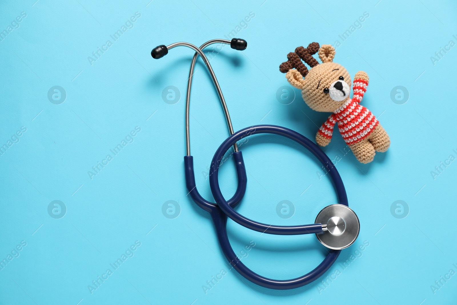 Photo of Pediatrics concept. Toy deer with stethoscope on light blue background, top view. Space for text