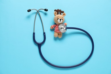 Photo of Pediatrics concept. Toy deer with stethoscope on light blue background, top view