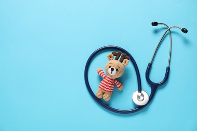 Photo of Pediatrics concept. Toy deer with stethoscope on light blue background, top view. Space for text