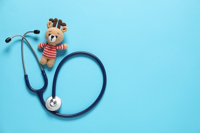 Photo of Pediatrics concept. Toy deer with stethoscope on light blue background, top view. Space for text