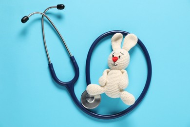 Photo of Pediatrics concept. Toy bunny with stethoscope on light blue background, top view