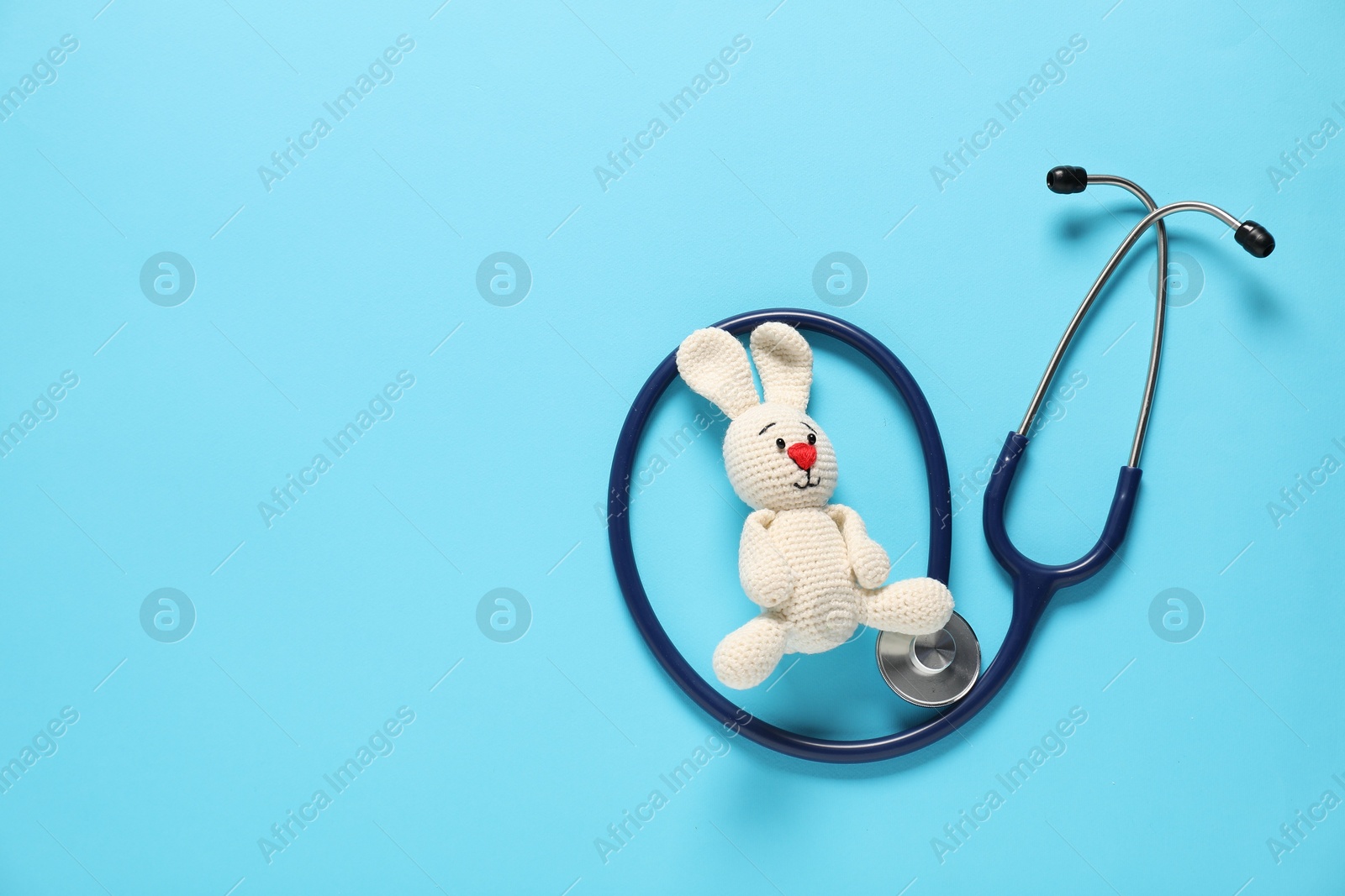 Photo of Pediatrics concept. Toy bunny with stethoscope on light blue background, top view. Space for text