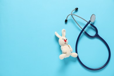 Photo of Pediatrics concept. Toy bunny with stethoscope on light blue background, top view. Space for text