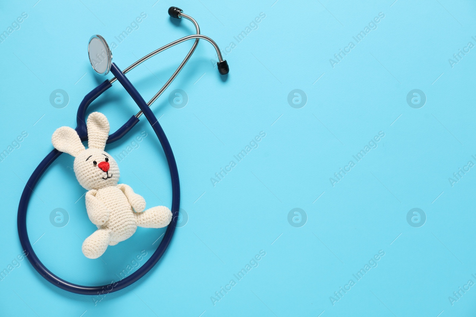 Photo of Pediatrics concept. Toy bunny with stethoscope on light blue background, top view. Space for text