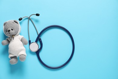 Photo of Pediatrics concept. Toy bear with stethoscope on light blue background, top view. Space for text