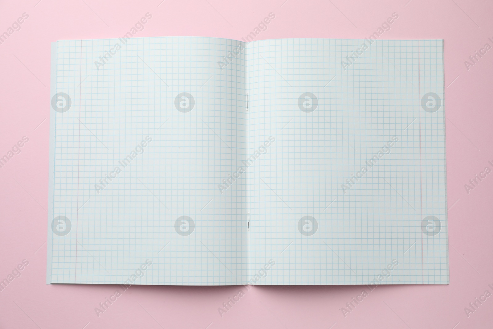 Photo of Open copybook with checkered sheets of paper on pink background, top view. School stationery