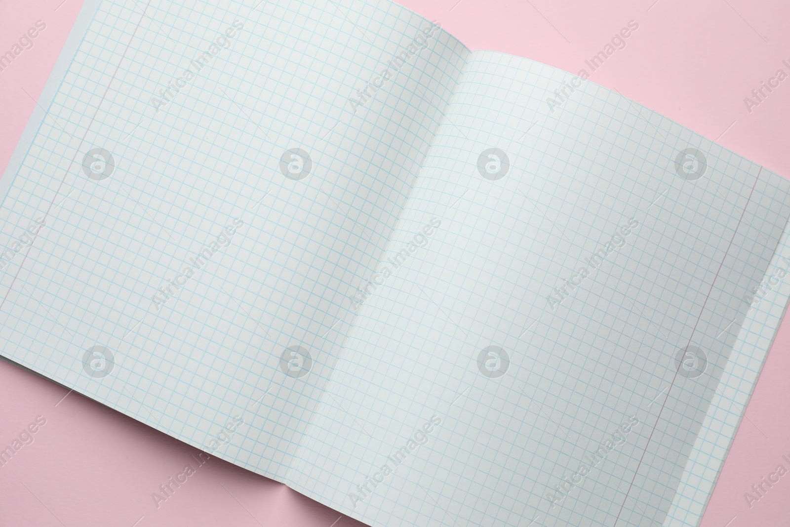 Photo of Open copybook with checkered sheets of paper on pink background, top view. School stationery