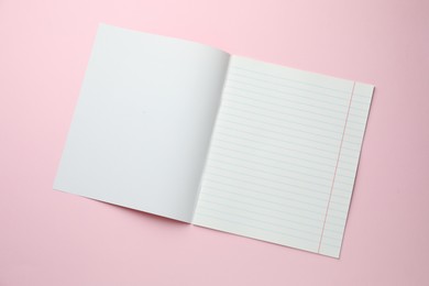 Photo of Open copybook on pink background, top view. School stationery